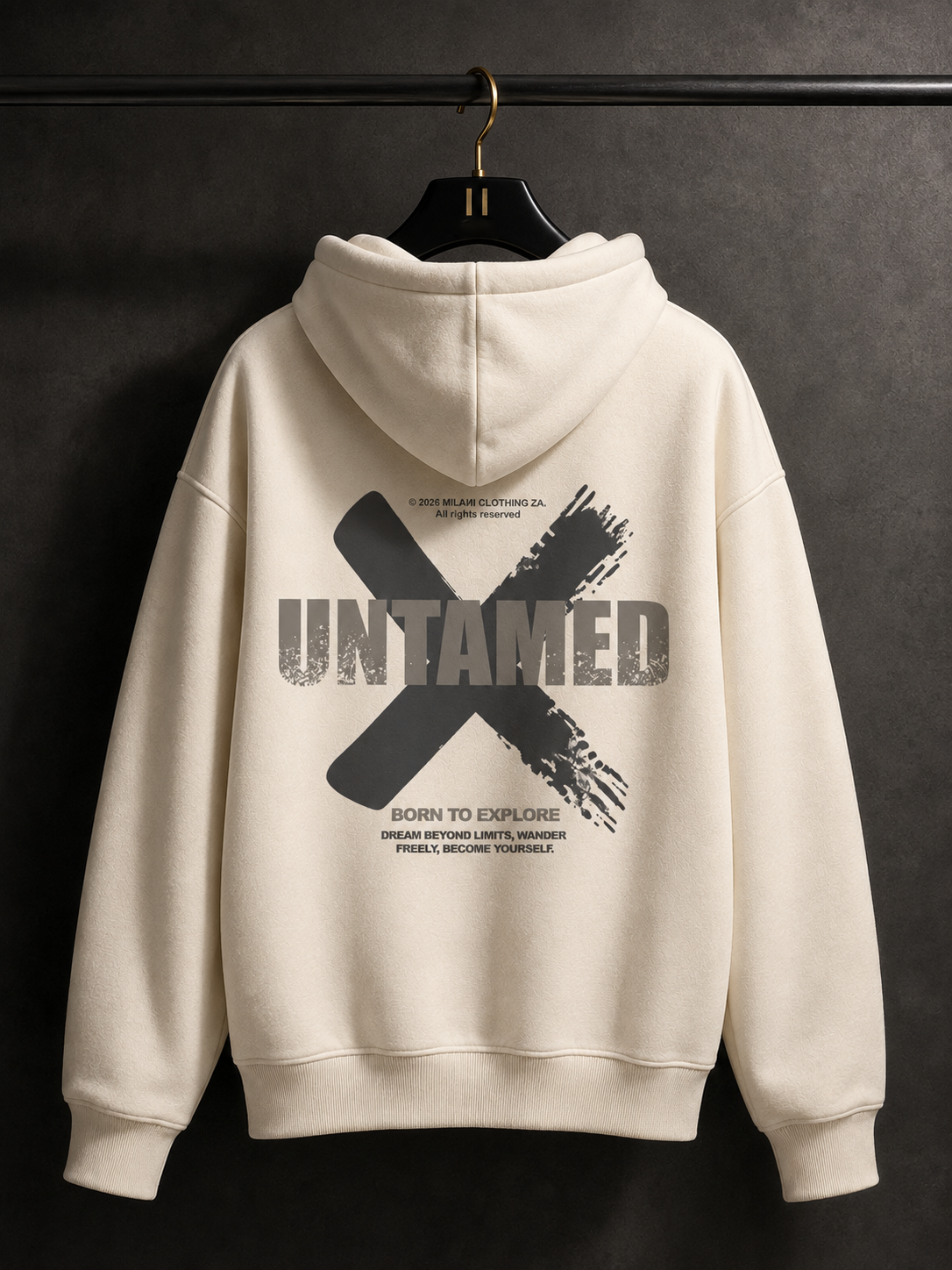 An off-white hooded sweatshirt hanging on a black hanger against a dark textured wall, showing the back with a large black graphic print featuring the word 'UNTAMED' and smaller text.