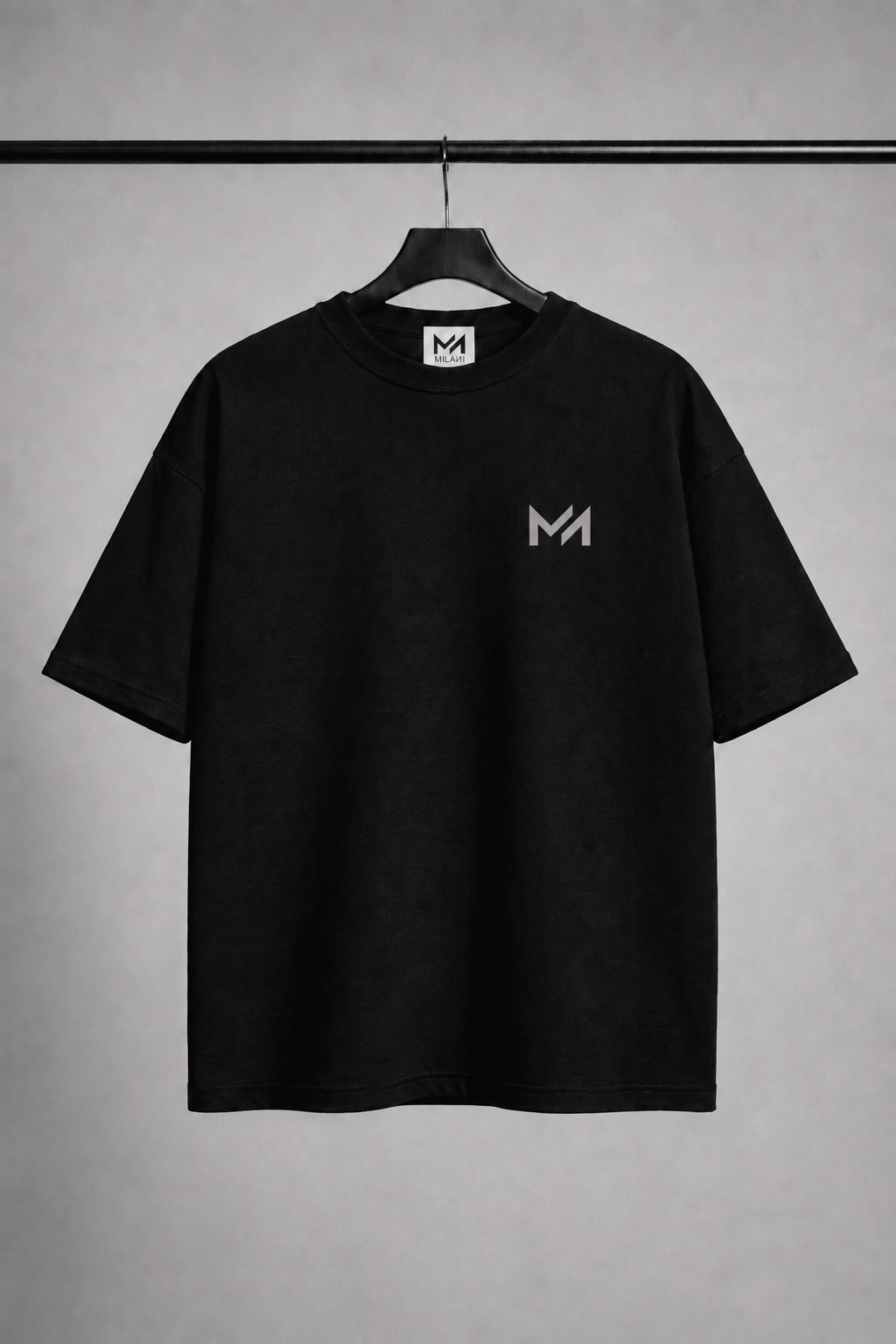 A black short-sleeve crewneck t-shirt hanging on a black hanger against a textured gray background. The shirt features a small light gray stylized 'MILAИI logo on the left chest and a matching 'MILAИI' logo printed inside the collar.