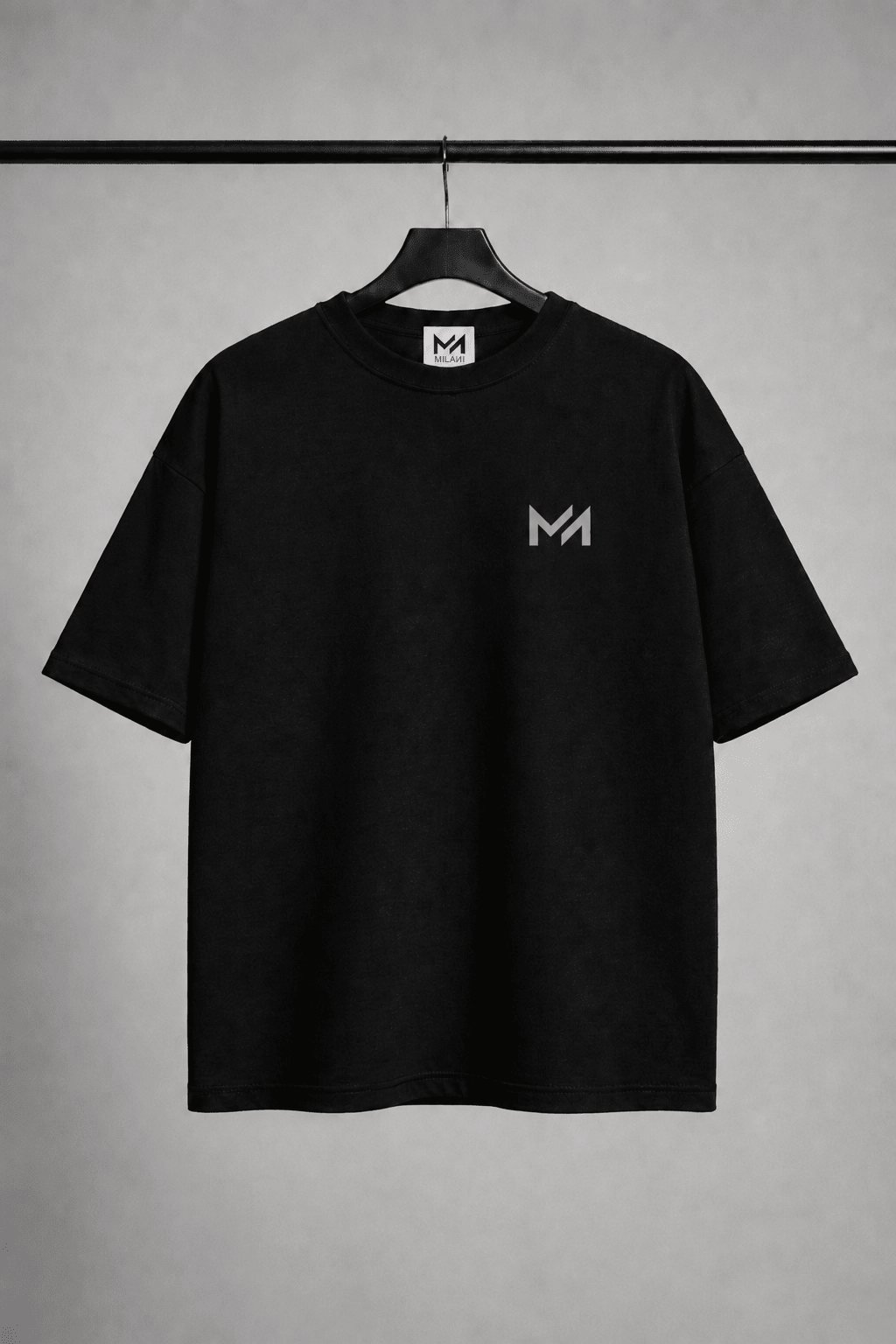 MILANI Born for Stardom Oversized T-Shirt – Black - MILANI CLOTHINGMILANI Born for Stardom Oversized T-Shirt – BlackChildren's Oversized T-ShirtsMILANI CLOTHINGMILANI CLOTHING2-3 yearsA black short-sleeve crewneck t-shirt hanging on a black hanger against a textured gray background. The shirt features a small light gray stylized 'MILAИI logo on the left chest and a matching 'MILAИI' logo printed inside the collar.