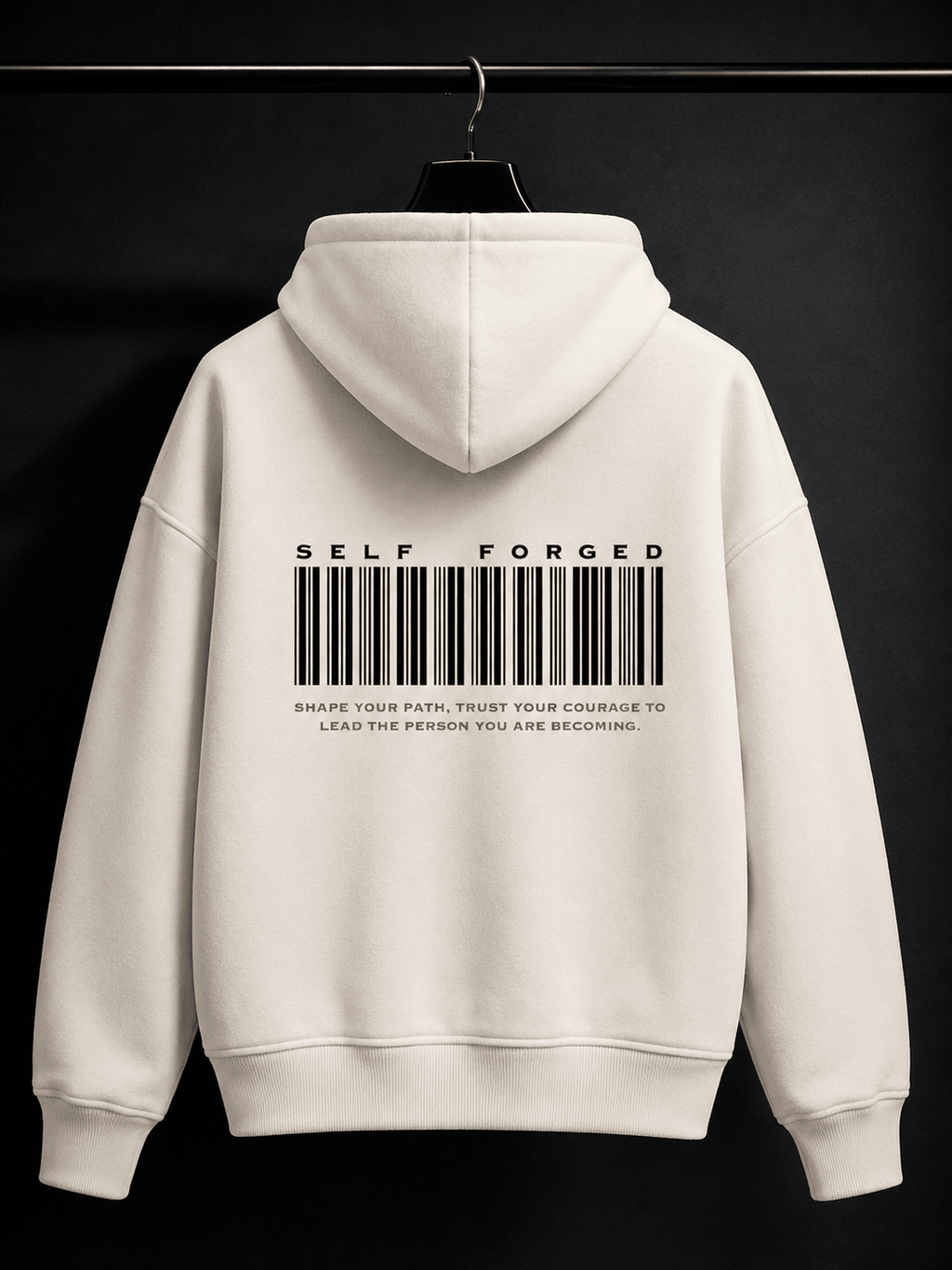 MILANI Self Forged Heavyweight Hoodie – Cream - MILANI CLOTHINGMILANI Self Forged Heavyweight Hoodie – CreamLoosefit Heavyweight hoodieMILANI CLOTHINGMILANI CLOTHING4-6 YearsAn off-white hoodie hanging on a black hanger against a dark background, featuring a black barcode graphic and the text 'SELF FORGED' printed on the back.
