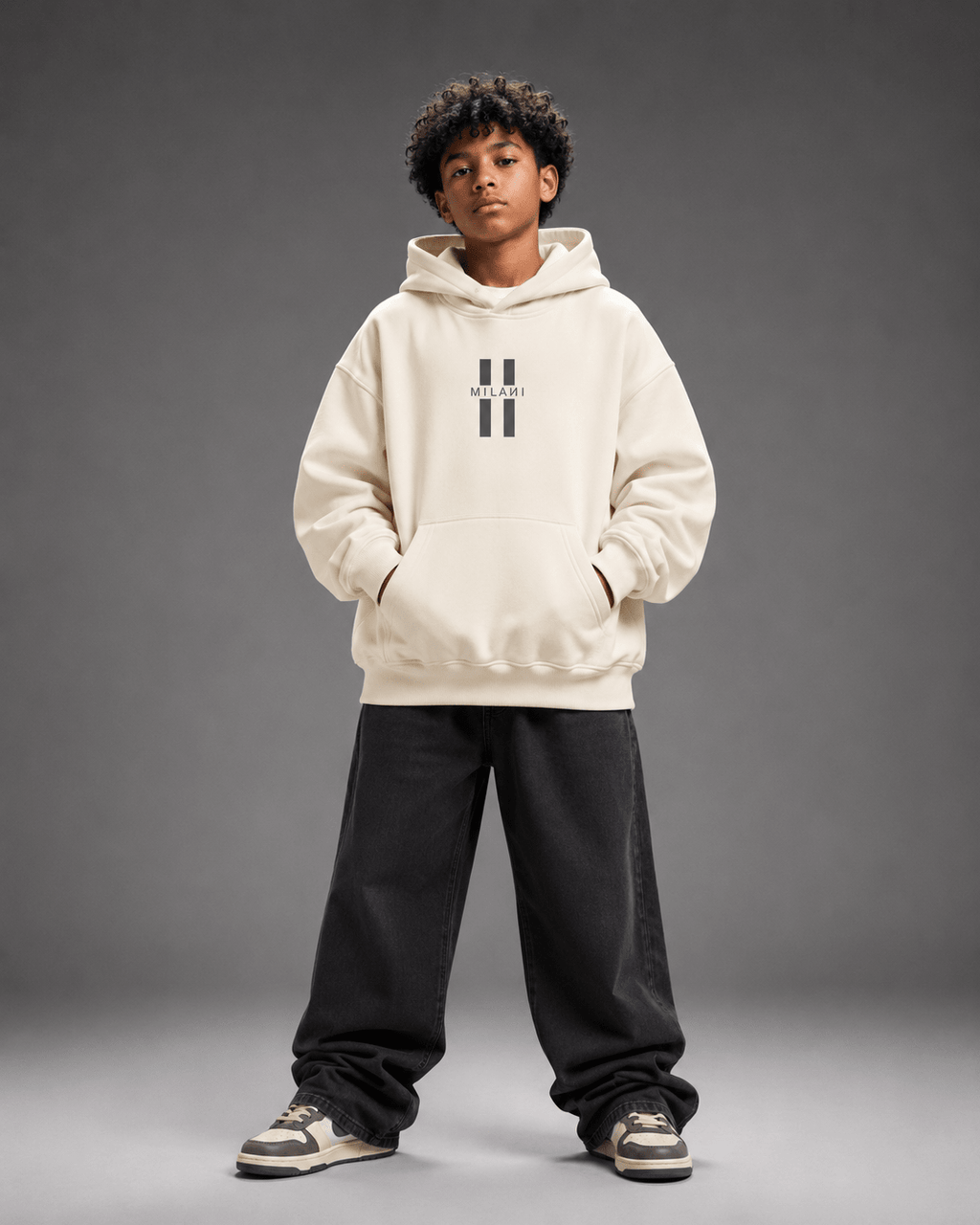 MILANI Untamed Heavyweight Kids Hoodie – Cream - MILANI CLOTHINGMILANI Untamed Heavyweight Kids Hoodie – CreamLoosefit Heavyweight hoodieMILANI CLOTHINGMILANI CLOTHING4-6 YearsA child model wearing a cream-colored hoodie with a black double-stripe logo on the chest, paired with black sweatpants and sneakers, standing against a dark gray studio background.